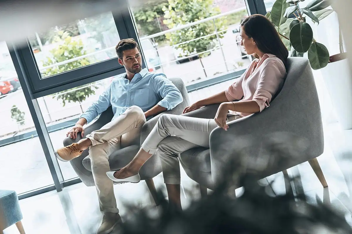 A man and woman seated in chairs engaged in a counseling session