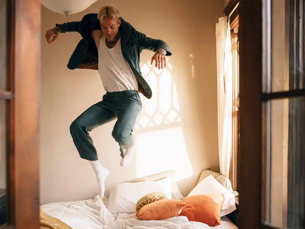 A man with ADHD leaps into the air on a bed, embodying a moment of playful spontaneity and vibrant energy.