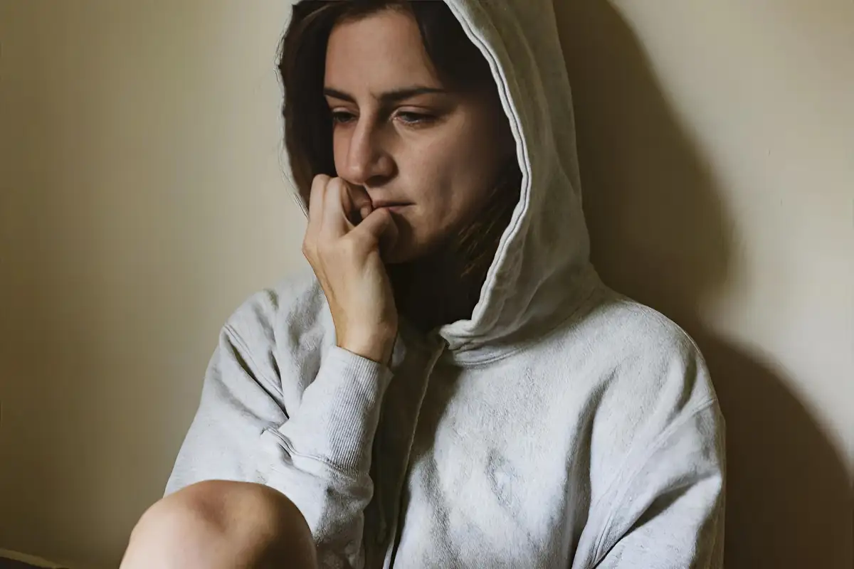 A woman in a hoodie sits on the floor with mental health issue