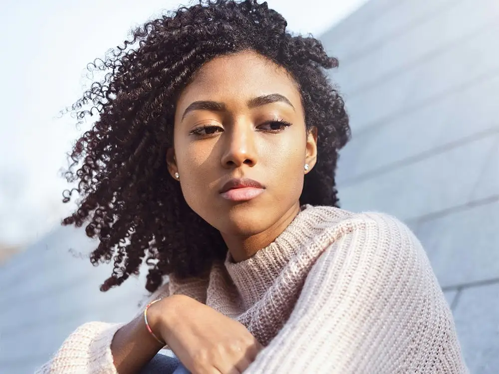 A woman with curly hair sits on a wall, reflecting on her journey through virtual mental health treatment programs