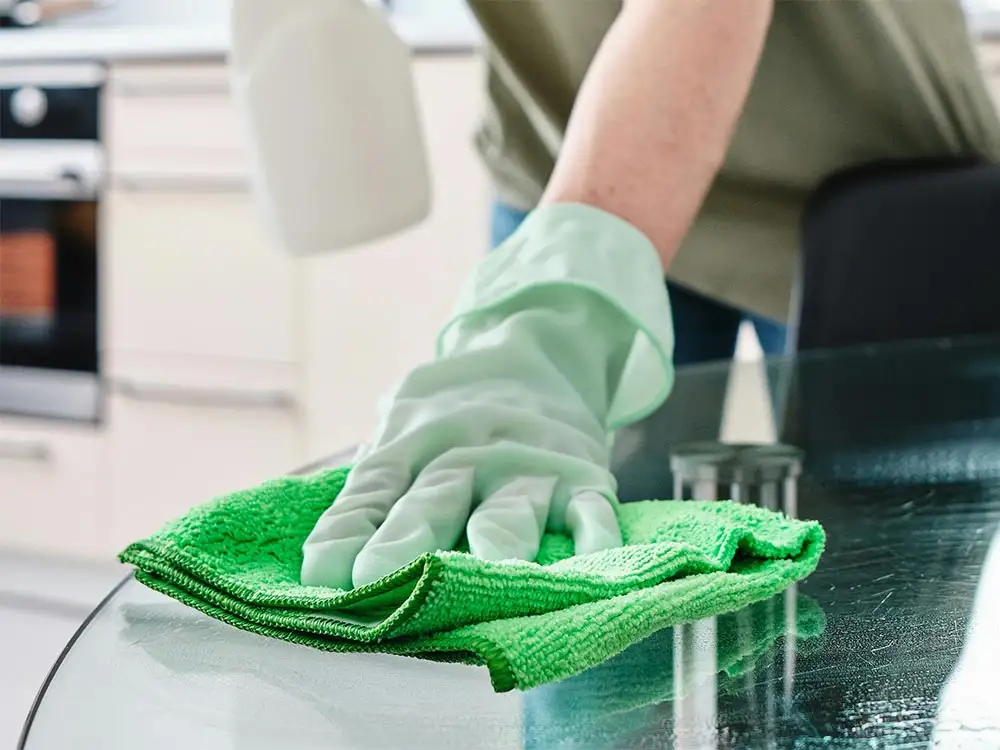 a woman with OCD wearing green cleaning gloves cleaning the table repeatedly