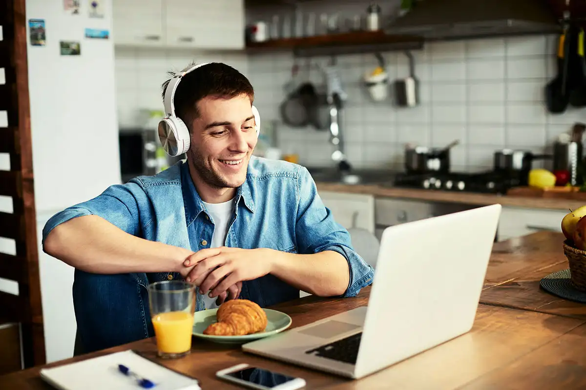 A man in headphones at a table with a laptop and orange juice, representing continuity of care in virtual mental health support