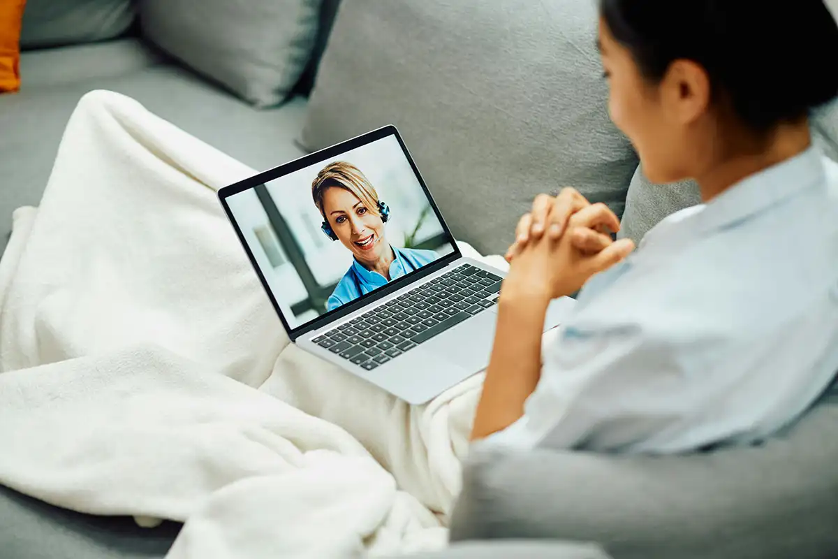 A woman on a couch uses her laptop for virtual therapy, highlighting a tailored approach to mental health support